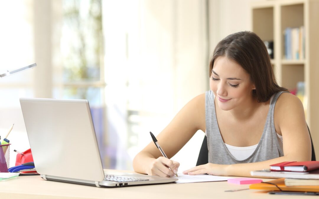 Beautiful student studying on line and learning writing notes in a desk at home